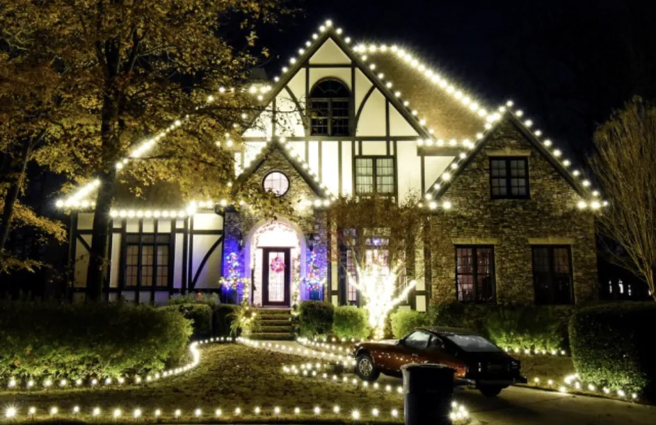 Tudor-style house with a tall arched dormer and lights along the front walkway.